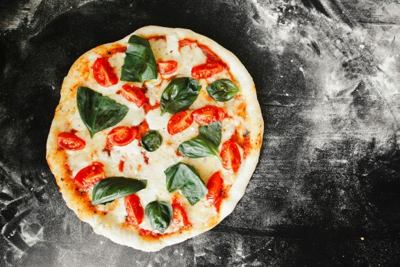 Pizza mit frischen Tomaten und Spinat auf einem dunklen Untergrund.
