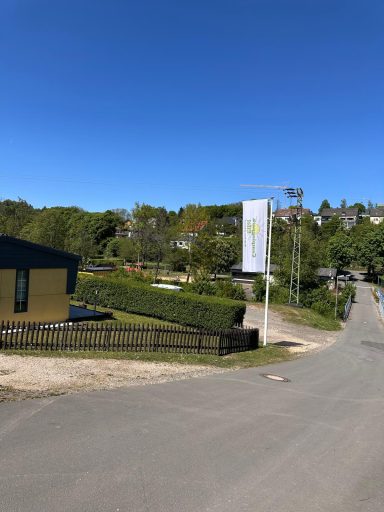 Zufahrt zum Capningplatz durch eine grüne Landschaft mit Bäumen und Willkommens-Schild.