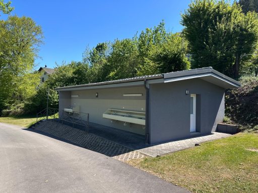 Modernes, graues Haus mit Spülbecken für Geschirr, mit großen Fenstern, umgeben von Bäumen und Wiese.
