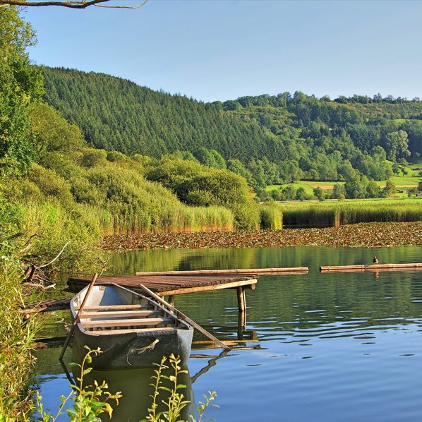 Ruhiger See mit einem kleinen Boot und grünen Ufern im Hintergrund.