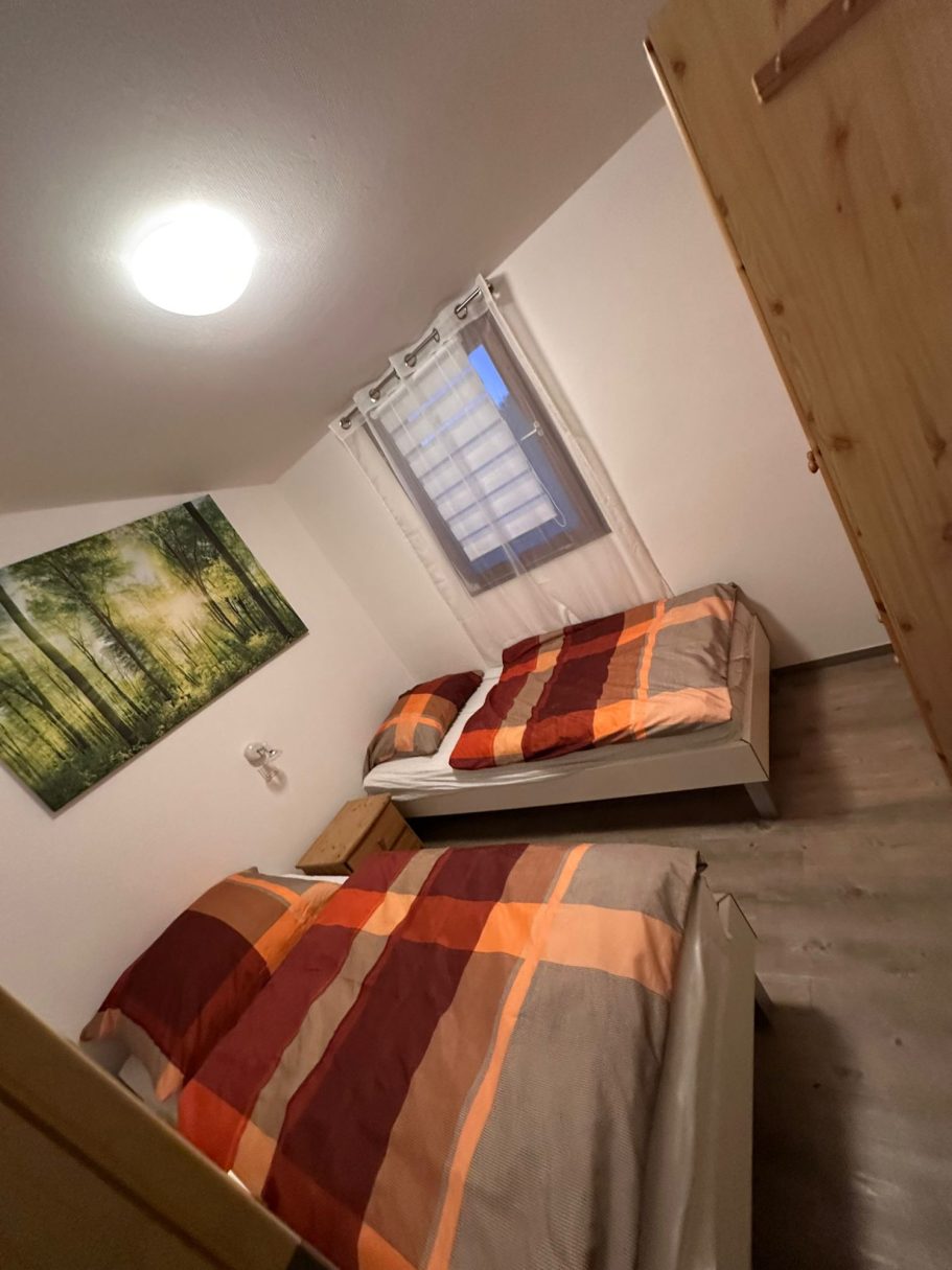 Das Schlafzimmer vom Ferienhaus Zimmer mit zwei Betten, Holzfußboden und Fensterblick auf einen Wald.