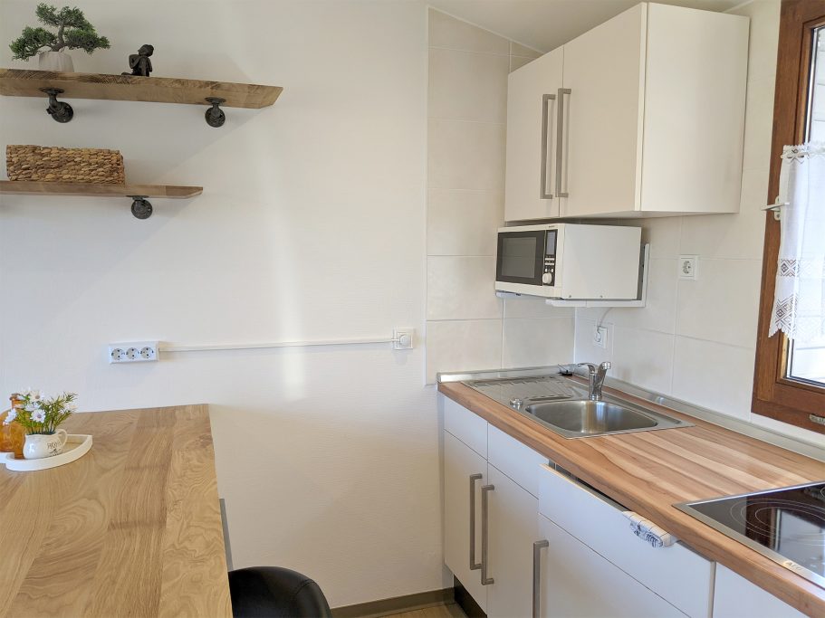 Küchenzeile im Ferienhaus Moderne Küche mit Holztisch, Spüle, Mikrowelle und offenen Regalen.