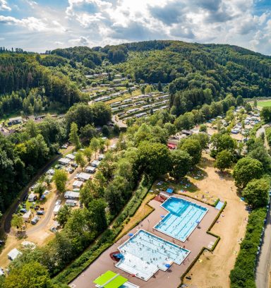 Luftaufnahme eines Campingplatzes mit Schwimmbad und umgebender Waldlandschaft.
