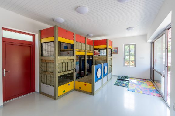 Raum mit farbenfrohen Spielgeräten und Teppich, beleuchtet durch natürliche Fenster.
