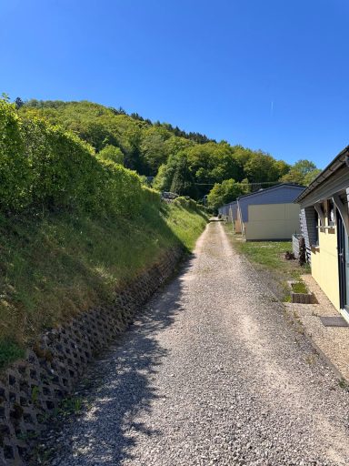 Schmale, kiesige Straße zwischen grünen Hügeln und niedrigen Gebäuden.