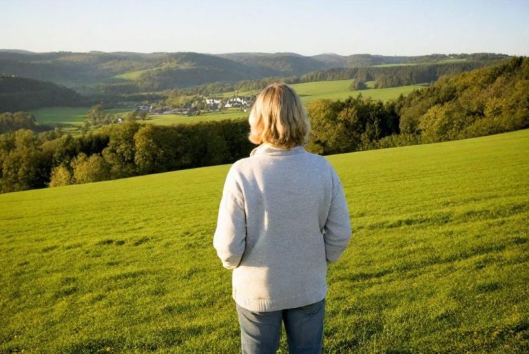 Wandern in der Eifel Eine Person mit blonden Haaren blickt über eine grüne Landschaft.