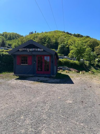 Kinderspielhaus mit Veranda vor einer grünen Hügelkulisse.