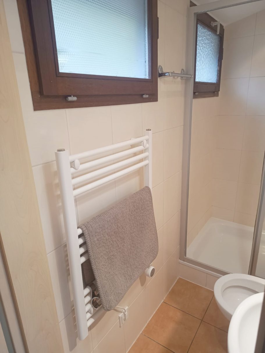 Das Bad vom Ferienhaus Weiße Handtuchheizung mit grauem Handtuch in einem Badezimmer neben einer Dusche.