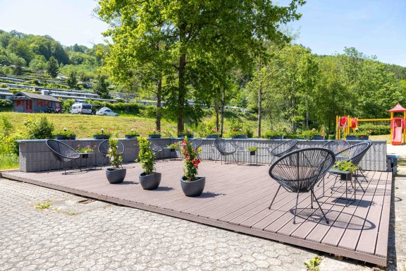 Terrasse mit Pflanzen und schwarzen Stühlen, umgeben von grüner Landschaft.