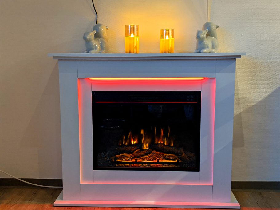 Wohnzimmer mit elektrischer Kamin mit Beleuchtung Weißer Kamin mit LED-Beleuchtung und zwei Kerzen auf der Ablage.