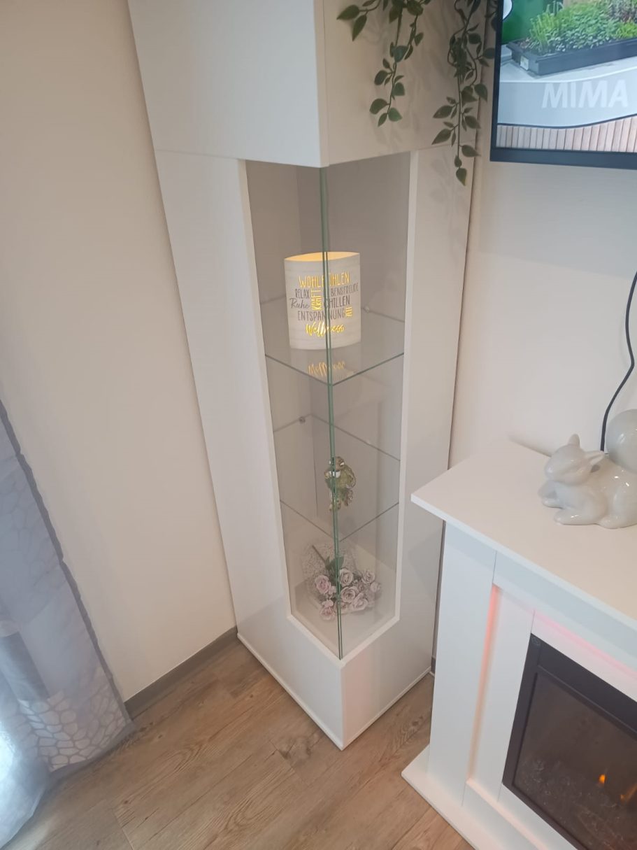Das Wohnzimmer vom Ferienhaus Eckvitrine mit Pflanze und dekorativem Licht, nahe einem Kamin.