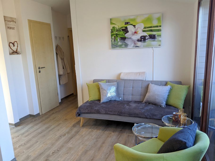 Das Wohnzimmer vom Ferienhaus Heller Wohnraum mit Sofa, Sessel offene Küche mit Esstresen und Kaminofen