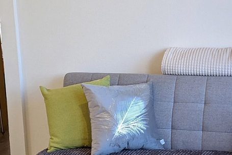 Das Sofa im Ferienhaus Bella Graue Couch mit bunten Kissen in Grün und Silber.